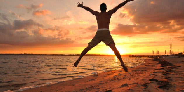 Young man jumping with spread arms celebrating and enjoying the moment at the seaside at sunset