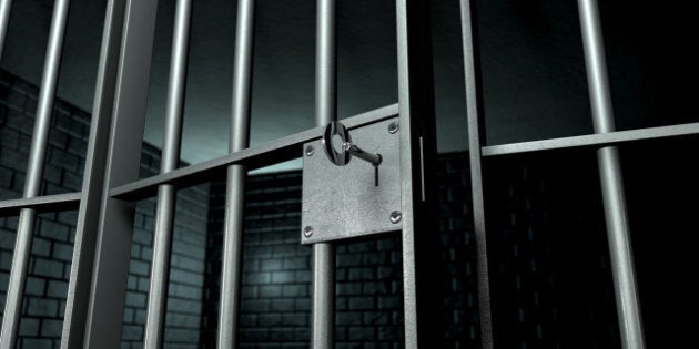 A closeup of the lock of a brick jail cell with iron bars and a key in the locking mechanism with the door open