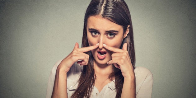 Closeup portrait headshot woman pinches nose with fingers hands looks with disgust something stinks bad smell situation isolated on gray wall background. Human face expression body language reaction.