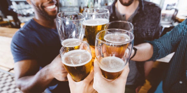 Multi ethnic group of friends toasting with beer glasses. High angle view, close up of hands. Unrecognizable people.