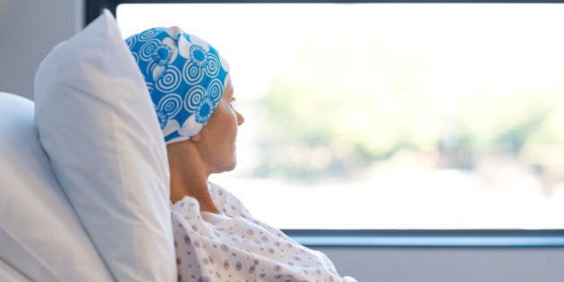 Young woman in bed suffering from cancer. Thoughtful woman battling with tumor looking out of window. Young patient with blue headscarf recovery in hospital on bed.