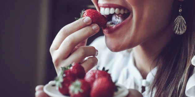 Young Latin woman tasting delicious strawberries. Close-up, candid shot.