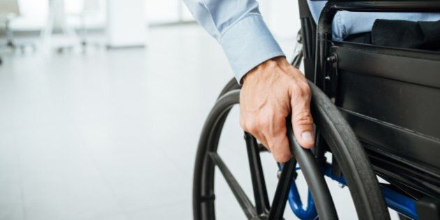Businessman in wheelchair, hand on wheel close up, office interior on background