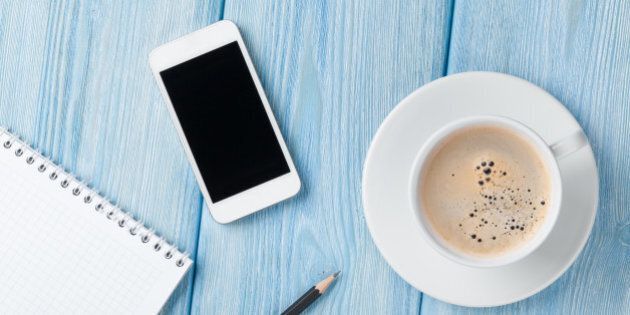 Coffee cup, smartphone and blank notepad on wooden table background. Top view with copy space