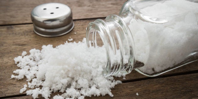 Spilled salt with salt shaker on wooden background