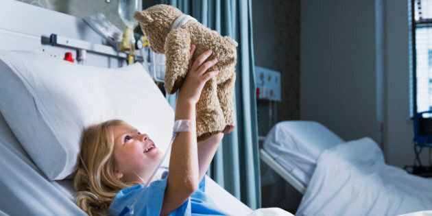 Little girl in a hospital bed playing and smiling to her Teddy Bear.