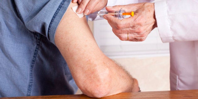 Senior man getting an injection from a nurse or doctor in the office. Doctor holds the syringe and has just finished and is wiping the injection site with alcohol.