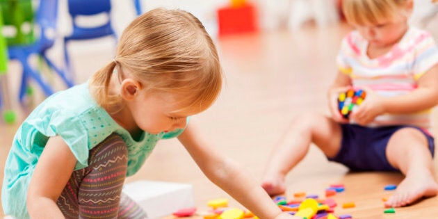 Two sweet Caucasian toddler girls playing with puzzle pieces on the floor of their preschool classroom. The puzzle pieces are colorful and the preschoolers are focused on the task at hand.