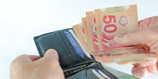 An used black leather wallet showingl a hand taking currency from it to make a purchase. Light background.