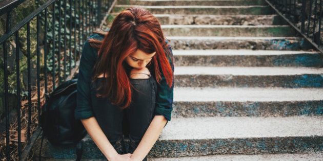 Depressed young woman sitting on stairs outdoors, with copy space