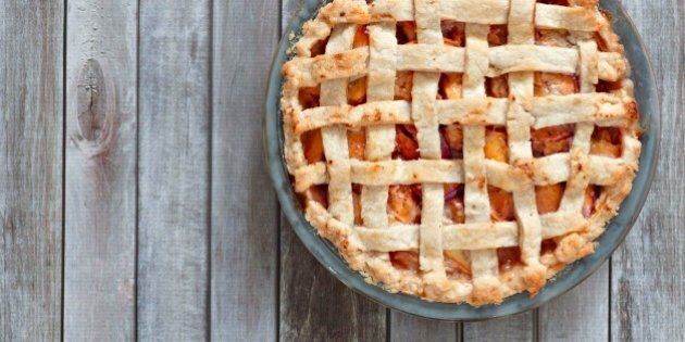Rustic homemade peach pie in baking plate, above view on a wood background