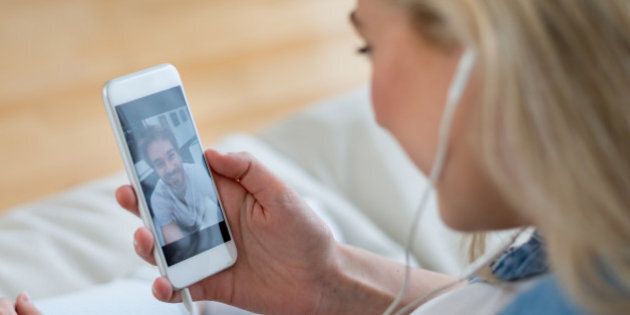 Woman at home video chatting with her boyfriend on her cell phone and using earphones