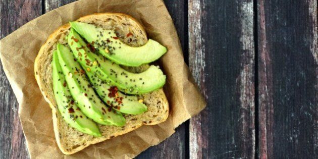 Open avocado sandwich with whole grain bread on paper against a rustic wooden background
