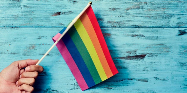 closeup of a young caucasian man waving a small rainbow flag against a rustic blue wooden background