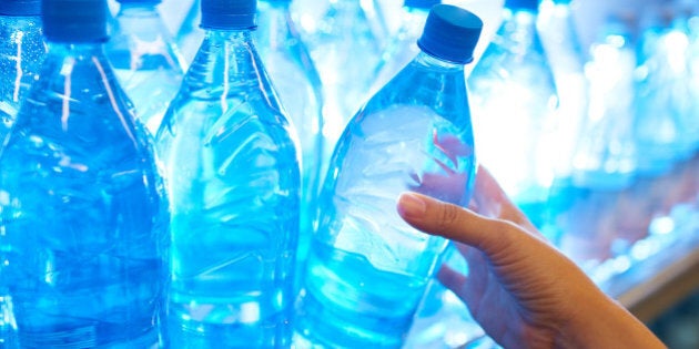 Human hand taking mineral water from shelf in supermarket