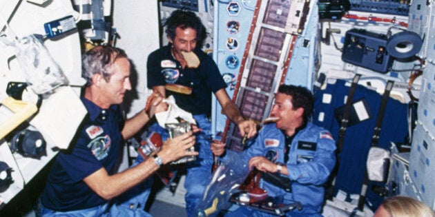 Astronauts eat a meal on board the Space Shuttle Discovery. Two of the astronauts hold slices of bread in their mouths. | Location: inside Space Shuttle Discovery, outer space. (Photo by © CORBIS/Corbis via Getty Images)