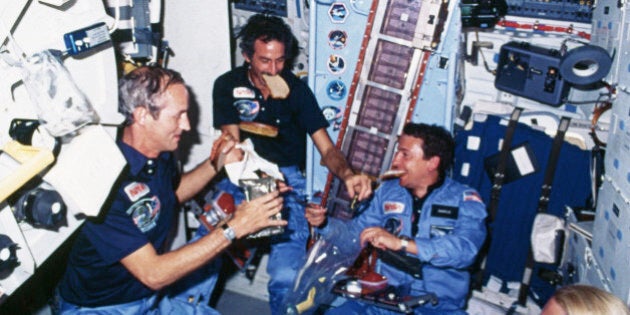 Astronauts eat a meal on board the Space Shuttle Discovery. Two of the astronauts hold slices of bread in their mouths. | Location: inside Space Shuttle Discovery, outer space. (Photo by Â© CORBIS/Corbis via Getty Images)