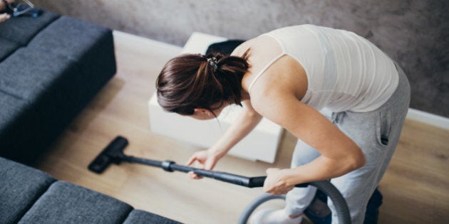 Woman cleaning the floor in living room with vacuum cleaner.