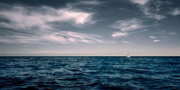 White sailing boat on water with wispy white clouds in sky