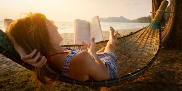 Young lady reading a book in hammock on a beach at sunset