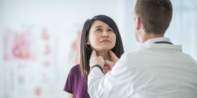 A multi-ethnic group of people are at the doctor's office. A doctor feels a woman's neck for any problems with her lymph nodes or thyroid.