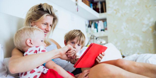 Mother with her sons watching tablet in bed