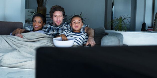 Multi-ethnic family having popcorn while watching TV in living room at home