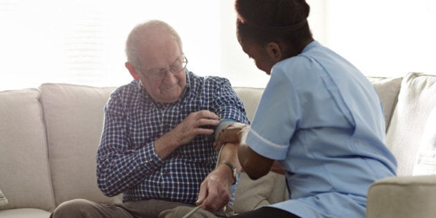 Home carer checking patients blood pressure at home on sofa