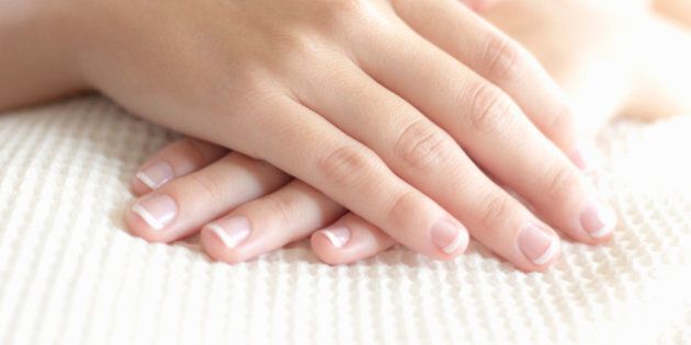 Woman folds her well manicured hands as she lays downs and enjoys a spa treatment