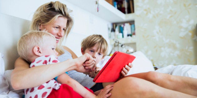 Mother with her sons watching tablet in bed