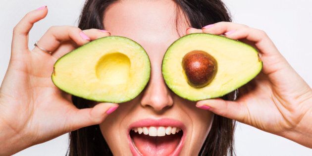 Beauty model holding avocado halves over her eyes