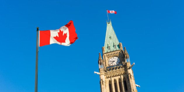Close up of peace tower (parliament building) with a big canadian flag over blue sky in Ottawa, Canada