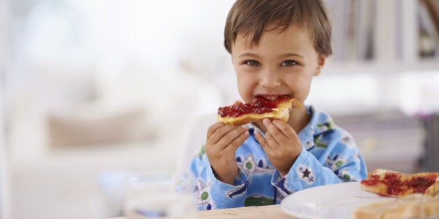 A cute little boy eating toast with jam