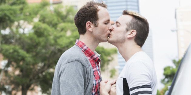 Gay men (20s, 30s) in city, kissing.