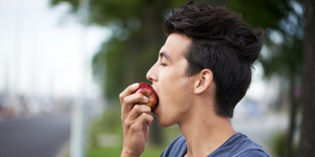 A young man taking a bite of an apple while waiting for the bus