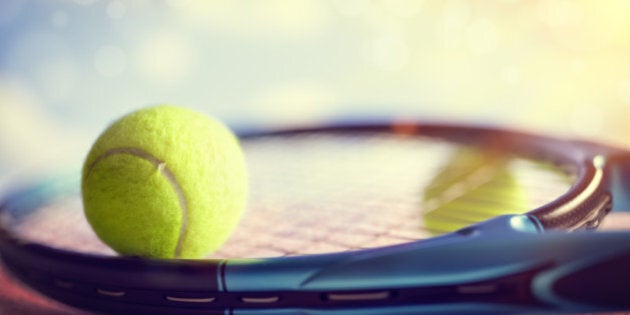 Tennis ball resting on top of a tennis racquet on a red asphalt court