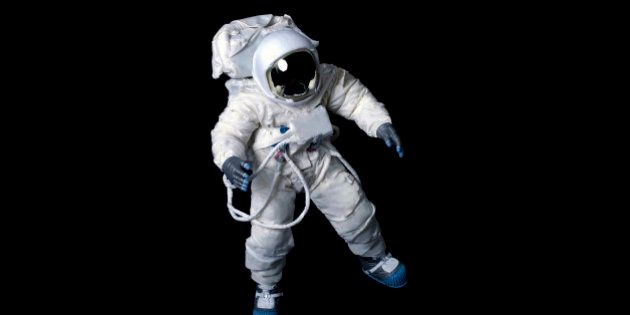 Astronaut wearing a plain pressure suit without symbols or insignia against a black background.