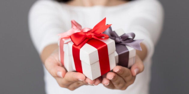 Woman holding a small gift box in a gesture of giving. Christmas holiday or special occasion gift box with red, purple and pink ribbon.