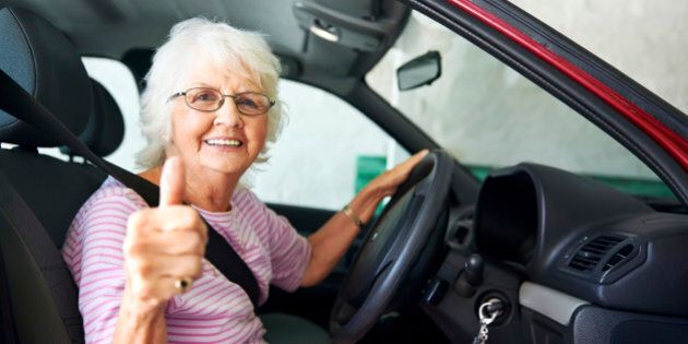 An positive older woman sitting in a car showing a thumbs up