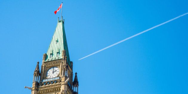Canadian Parliament Peace tower in Ottawa, with a plane over the blue sky and a white smoke trail