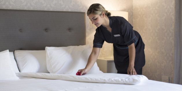 Chambermaid laying a flower onto the sheets while making a bed in a hotel room