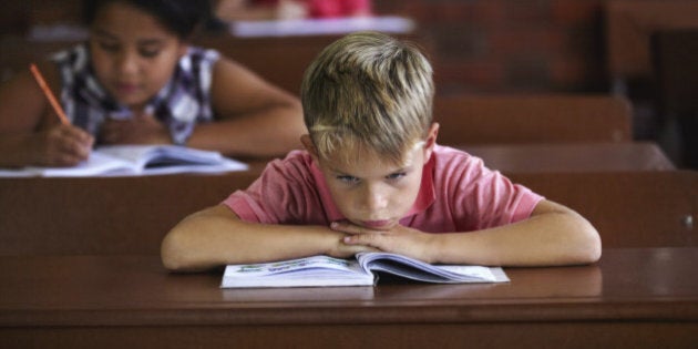 A young boy resting his head on his arms as he sits in a classroom looking bored