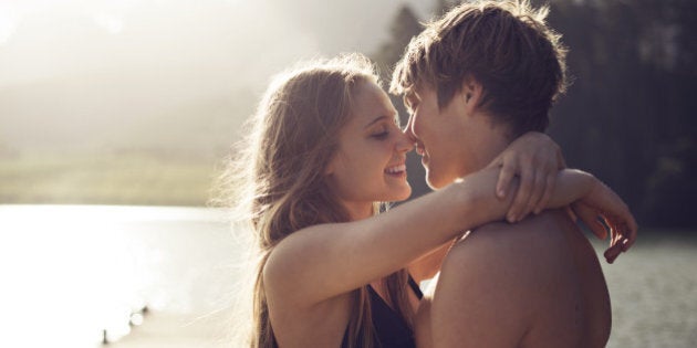 Young caucasian couple who are in love about to kiss next to a lake with the sun flaring