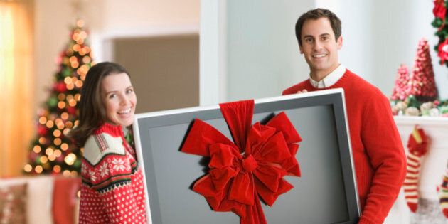 Couple holding flat screen TV with ribbon round it at Christmas