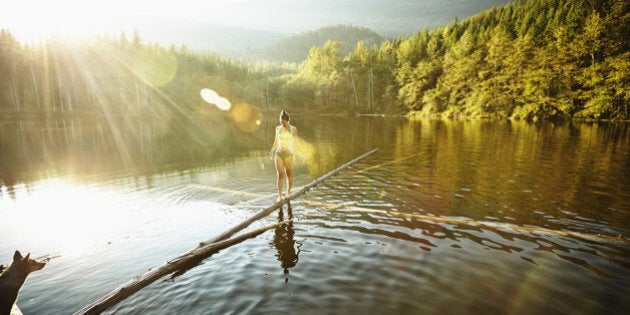 Woman walking on log in alpine lake with dog watching from dock