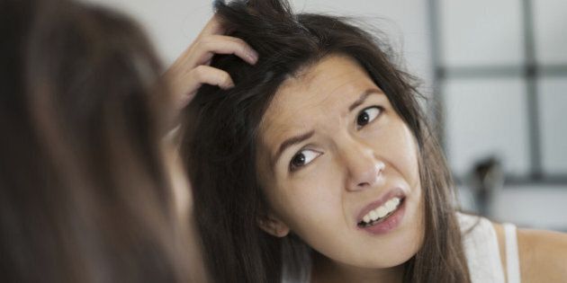 Woman having a bad hair day grimacing in disgust as she looks in the mirror and runs her hands through her hair