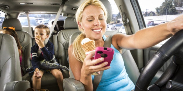 Soccer mom reads a text and eats an ice cream while driving her kids in minivan