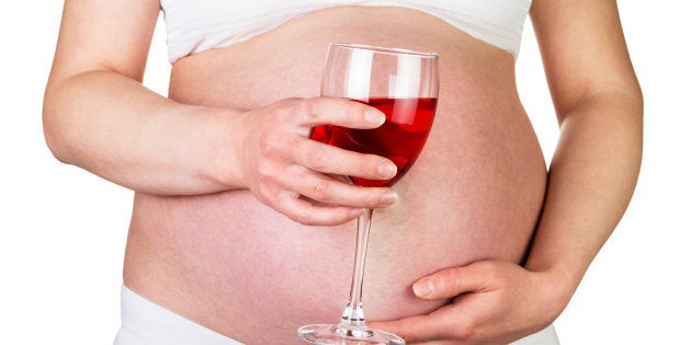 Pregnant woman holding a glass of red wine isolated on white background.