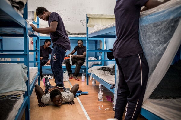 Abdullah, un jeune Gambien âgé de 15 ans (debout), aide son ami Alieu, âgé de 17 ans (au centre, étendu sur le plancher), à soulager ses douleurs au dos, dans un centre de réception pour les demandeurs d'asile qui sert également de centre d'hébergement pour les mineurs non-accompagnés, dans le port de Pozzallo, Sicile, en Italie (Mai 2016).