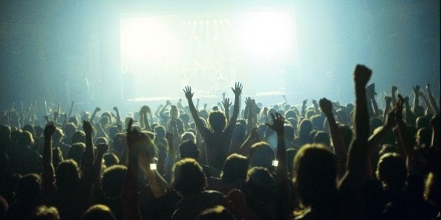 A general view of a rock concert taken from the back fo a venue showing the audience in silhouette raising their arms and cheering with bright lights shining from the stage, circa 1980. (Photo by Fin Costello/Redferns)